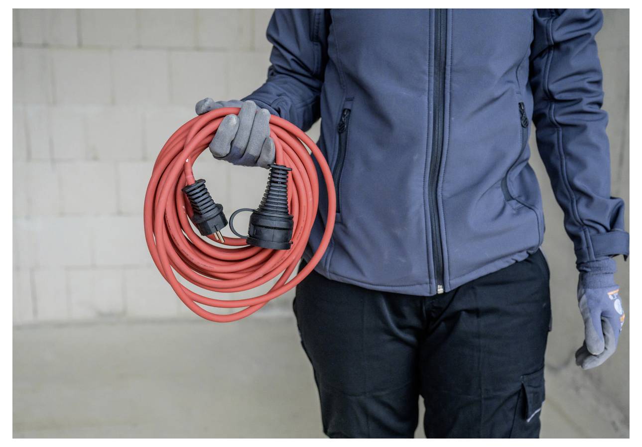 Ein Techniker in einer blauen Jacke und Handschuhen hält ein tragbares Schweißgerät und eine verbundene Steuereinheit, trägt einen Schultergurt und Arbeitshosen.