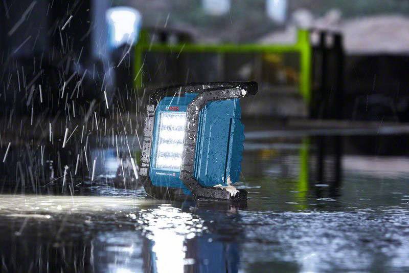 Eine Baustellenleuchte steht in einem nassen Raum. Wasser spritzt um die Leuchte, die für den Einsatz in feuchtem Umfeld geeignet ist.