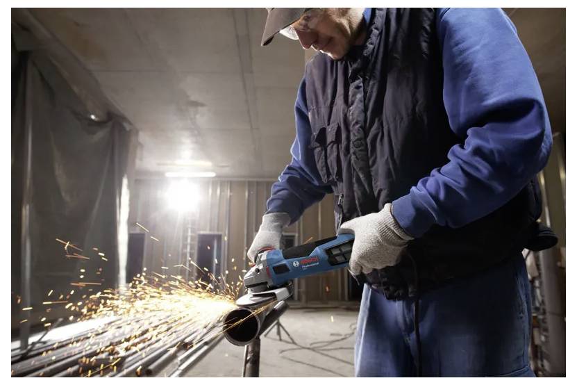 Eine Person verwendet eine Winkelschleifmaschine, um Metallrohre zu schneiden, wobei in einer Werkstattumgebung Funken entstehen.