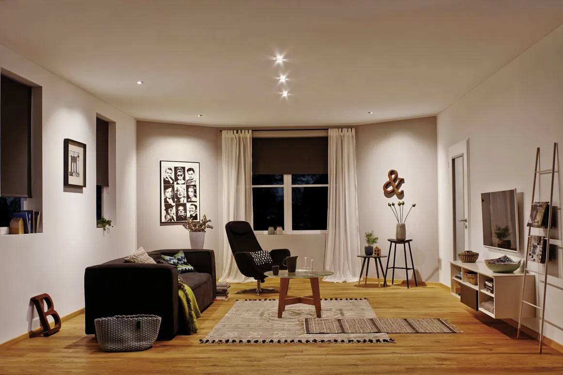 Ein modernes Wohnzimmer mit einer Couch, Sessel, Teppichen und Kunst an den Wänden. Es hat warme Beleuchtung und Holzboden.