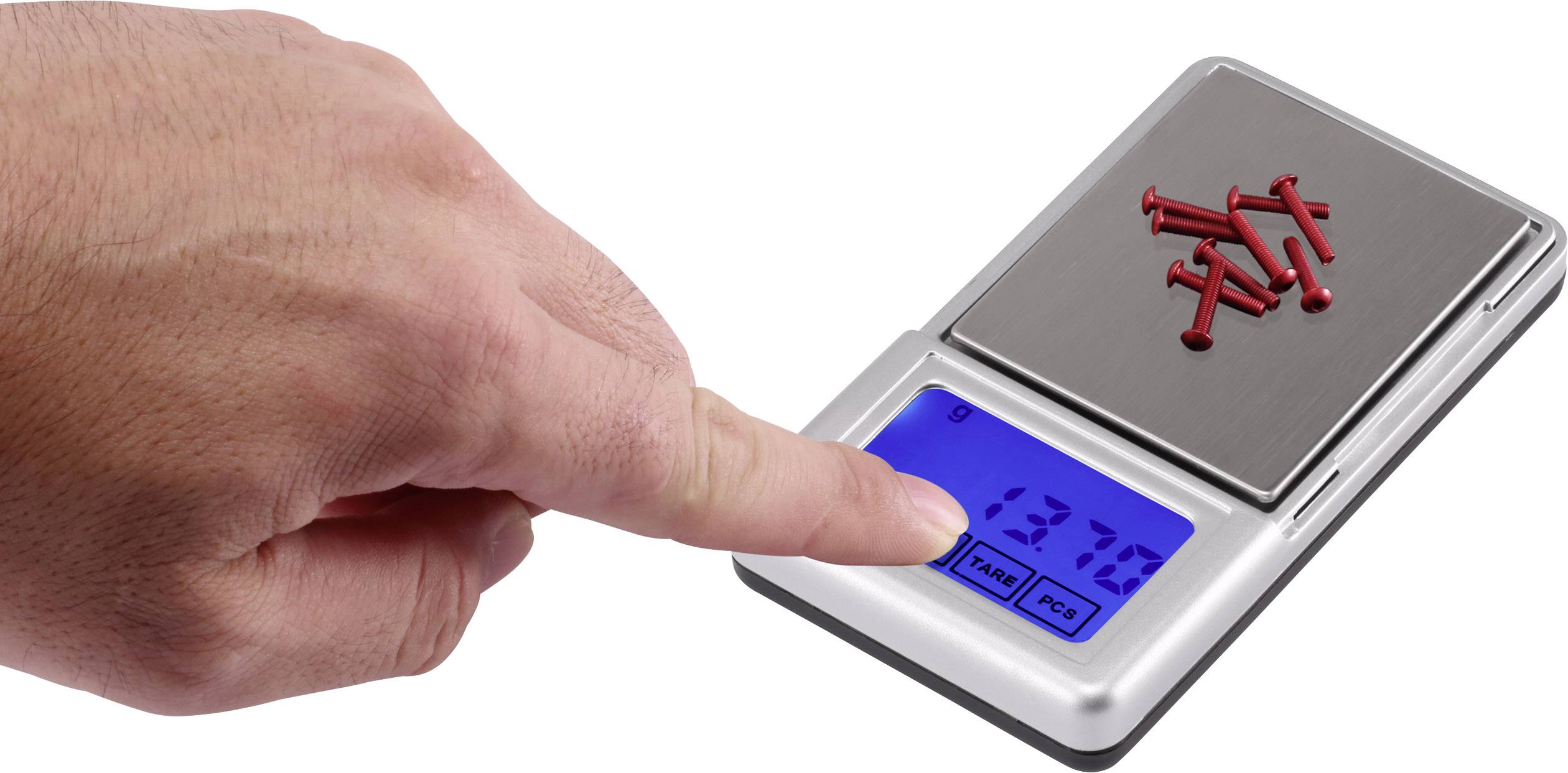 Eine Hand drückt auf eine digitale Waage, die kleine rote Nägel wiegt. Das Display zeigt '137.0'.