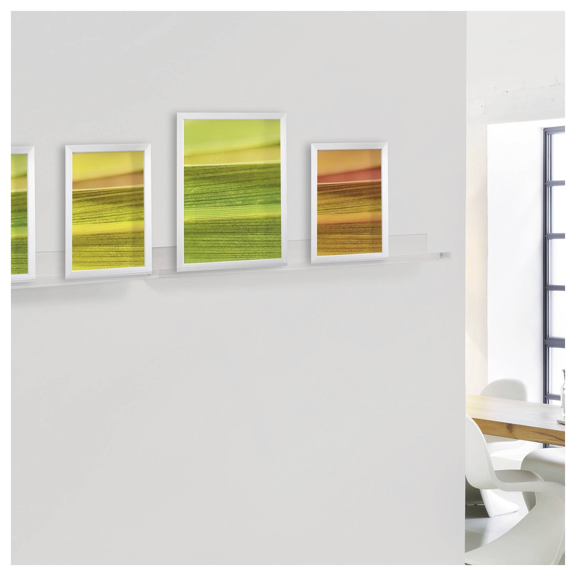 Eine minimalistische Galeriewand mit vier gerahmten abstrakten Landschaftsdrucken in Gelb, Grün und Orange neben einem hellen Essbereich.