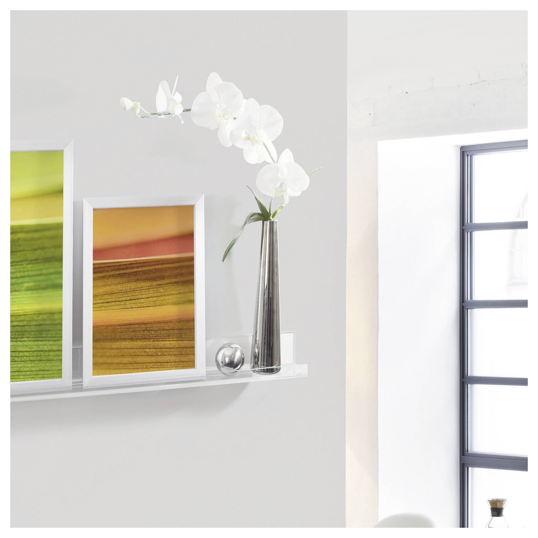 Minimalistische Wandleiste mit gerahmetem abstraktem Kunstwerk, einer silbernen Vase mit weißen Orchideen und einem hohen Fenster oder Spiegel rechts.