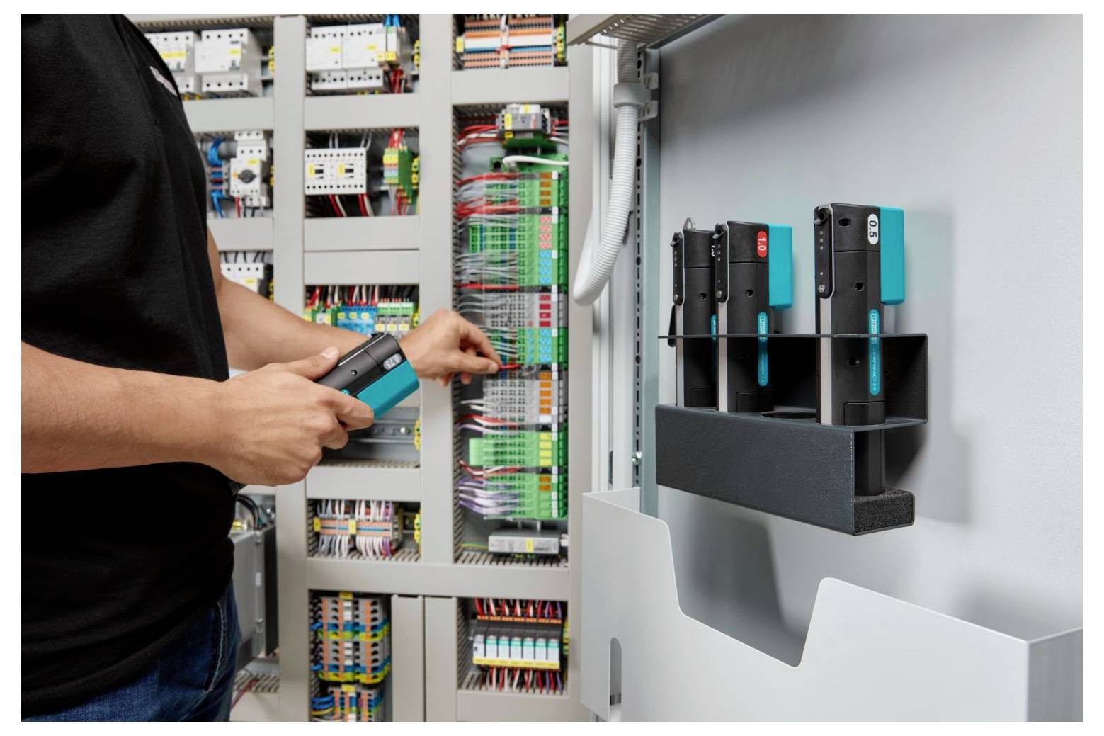 Techniker testet Verkabelung in einem offenen elektrischen Steuerschrank mit montierten Industriegeräten.