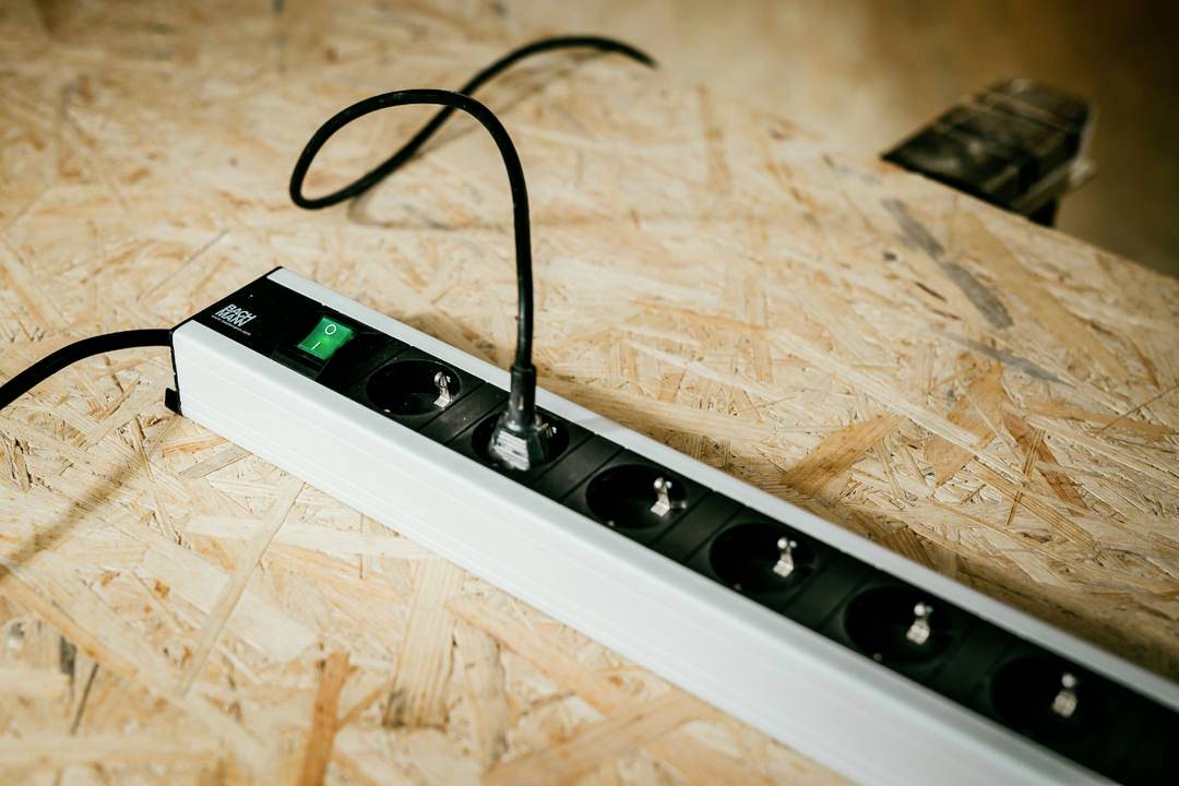 Steckerleiste mit mehreren Steckdosen, ein Kabel eingesteckt, auf einer Holzoberfläche.
