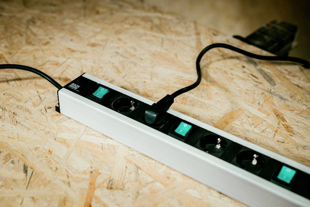 Eine Mehrfachsteckdose mit mehreren Steckdosen und Schaltern ruht auf einer Holzoberfläche, ein Kabel ist angesteckt, umgeben von hellen Holzspänen.