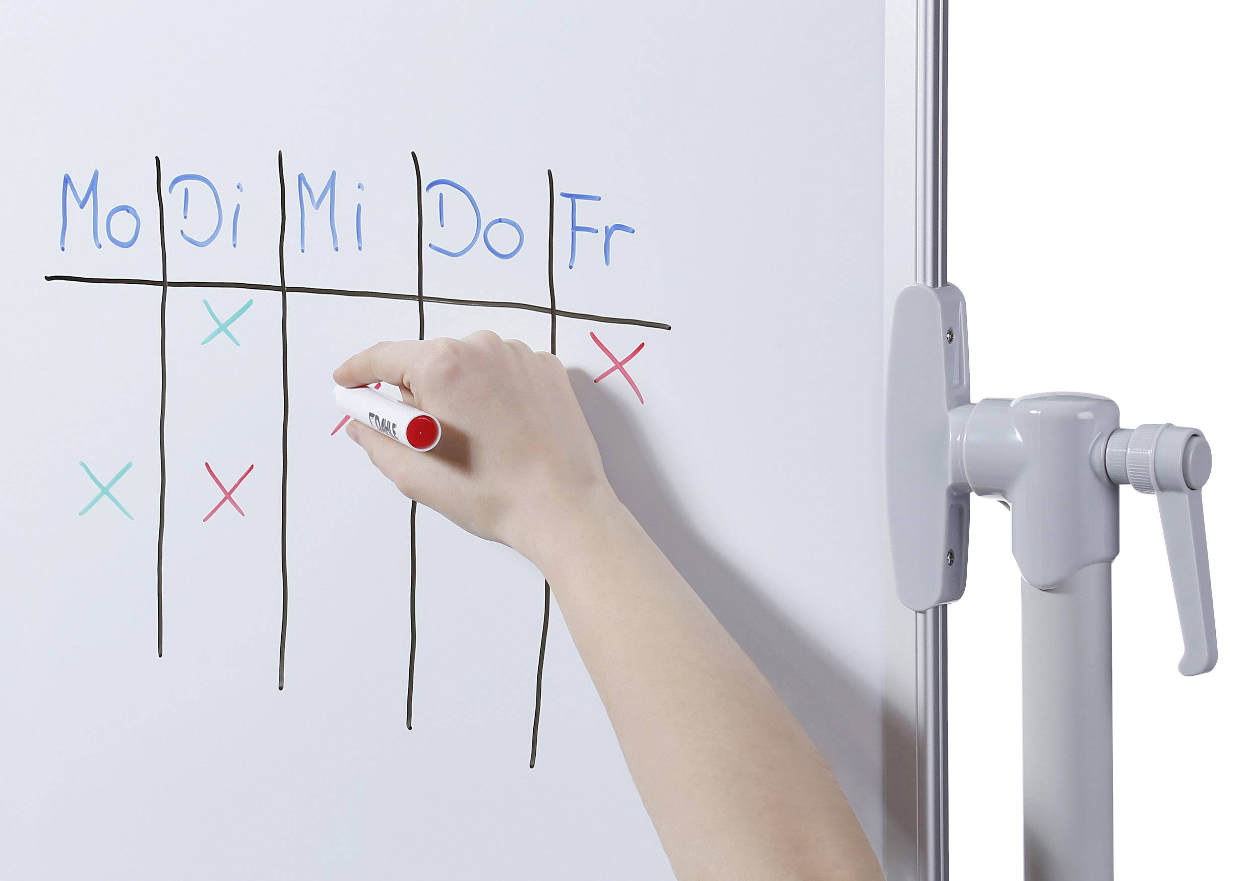 Eine Hand zeichnet mit einem roten Marker Kreuzchen in einer Tabelle mit den Wochentagen Montag bis Freitag auf einem Whiteboard.