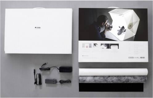 Fotostudio-Kit: Aufbewahrungsbox, Fotograf neben Mini-Fotostudio mit beleuchtetem Schuh, zwei Netzteile, Hintergrundrolle.