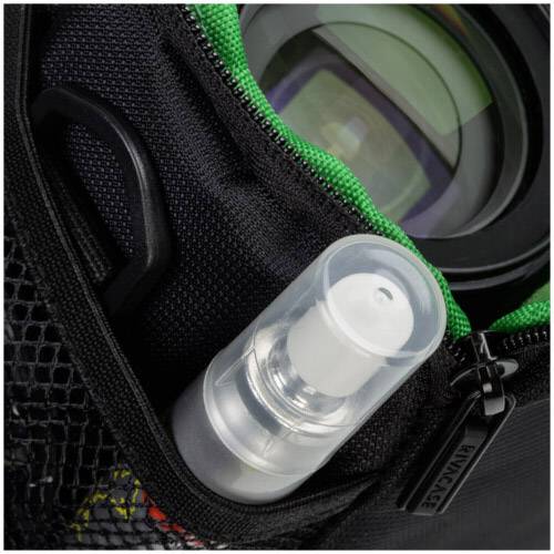 Eine kleine Sprühflasche und eine Kameralinse in einer Tasche mit grünem Reißverschluss und Netzfach.