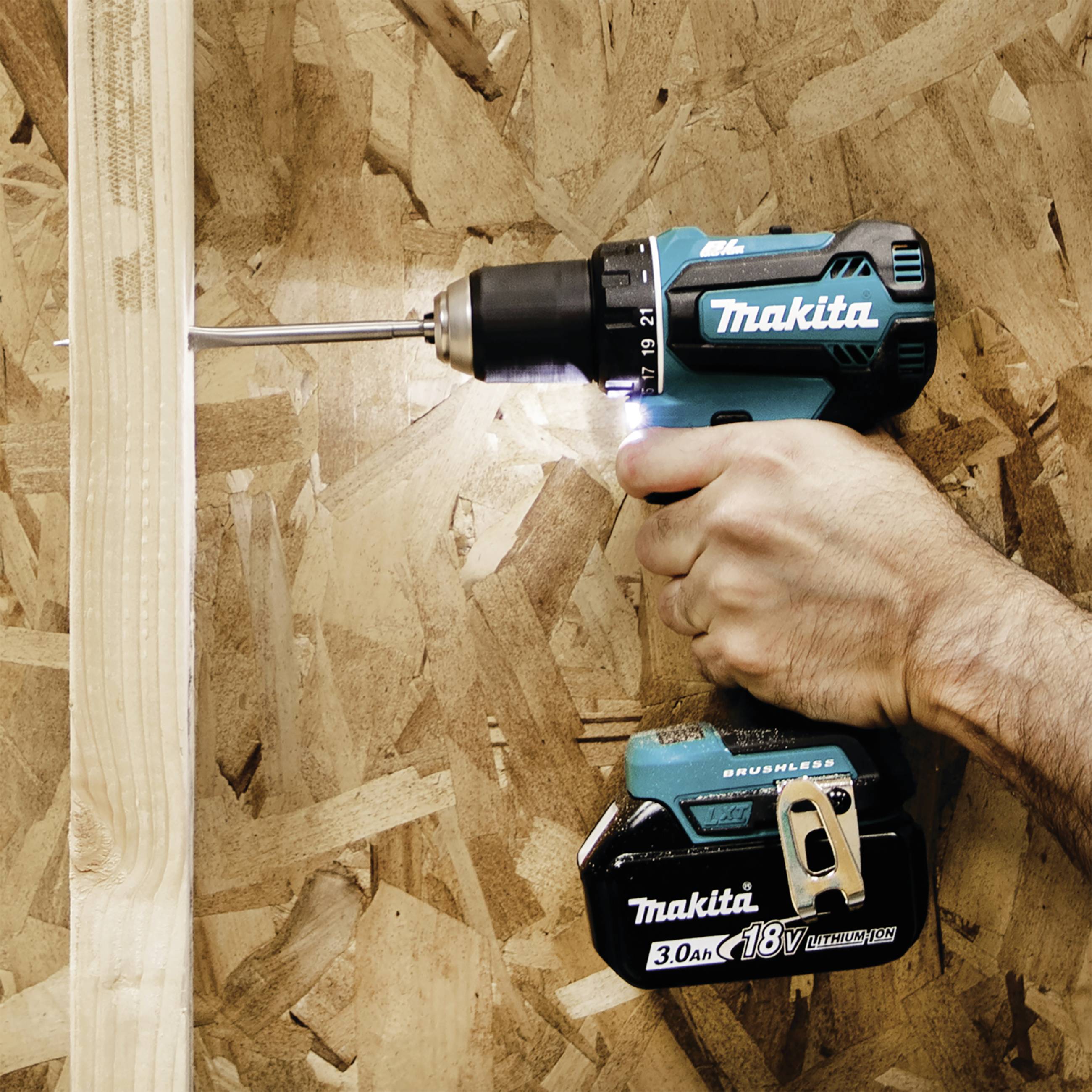 Eine Hand hält einen blauen Akkuschrauber, der in ein Holzbrett bohrt. Der Schrauber ist ein Makita-Modell mit 18V-Akku.