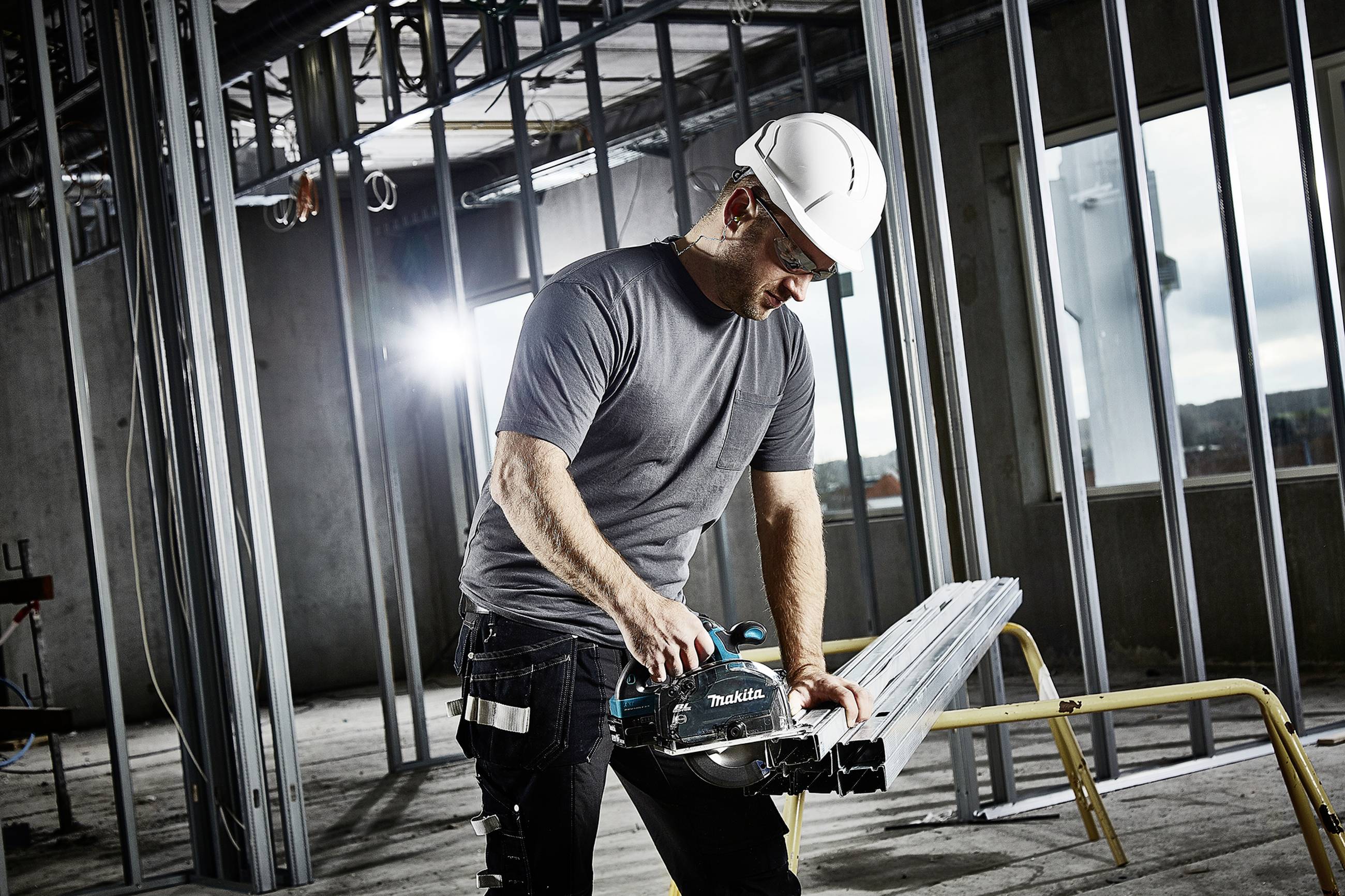 Arbeiter mit Schutzhelm verwendet eine elektrische Säge, um Metallstreben in einem unfertigen Gebäude zu schneiden. Hintergrund Baustelle.