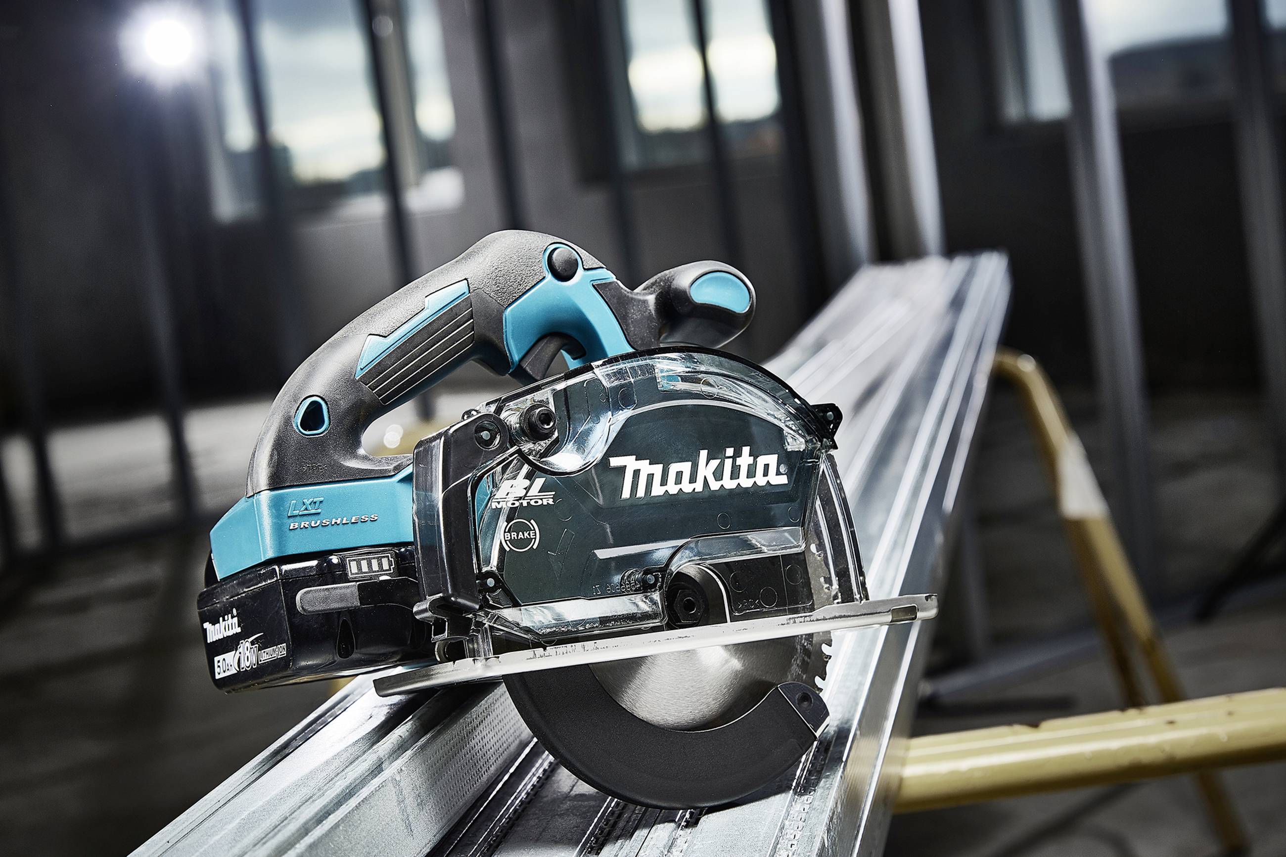 Handkreissäge der Marke Makita schneidet durch ein Metallstück, nah aufgenommen in einer Werkstattumgebung mit unscharfem Hintergrund.