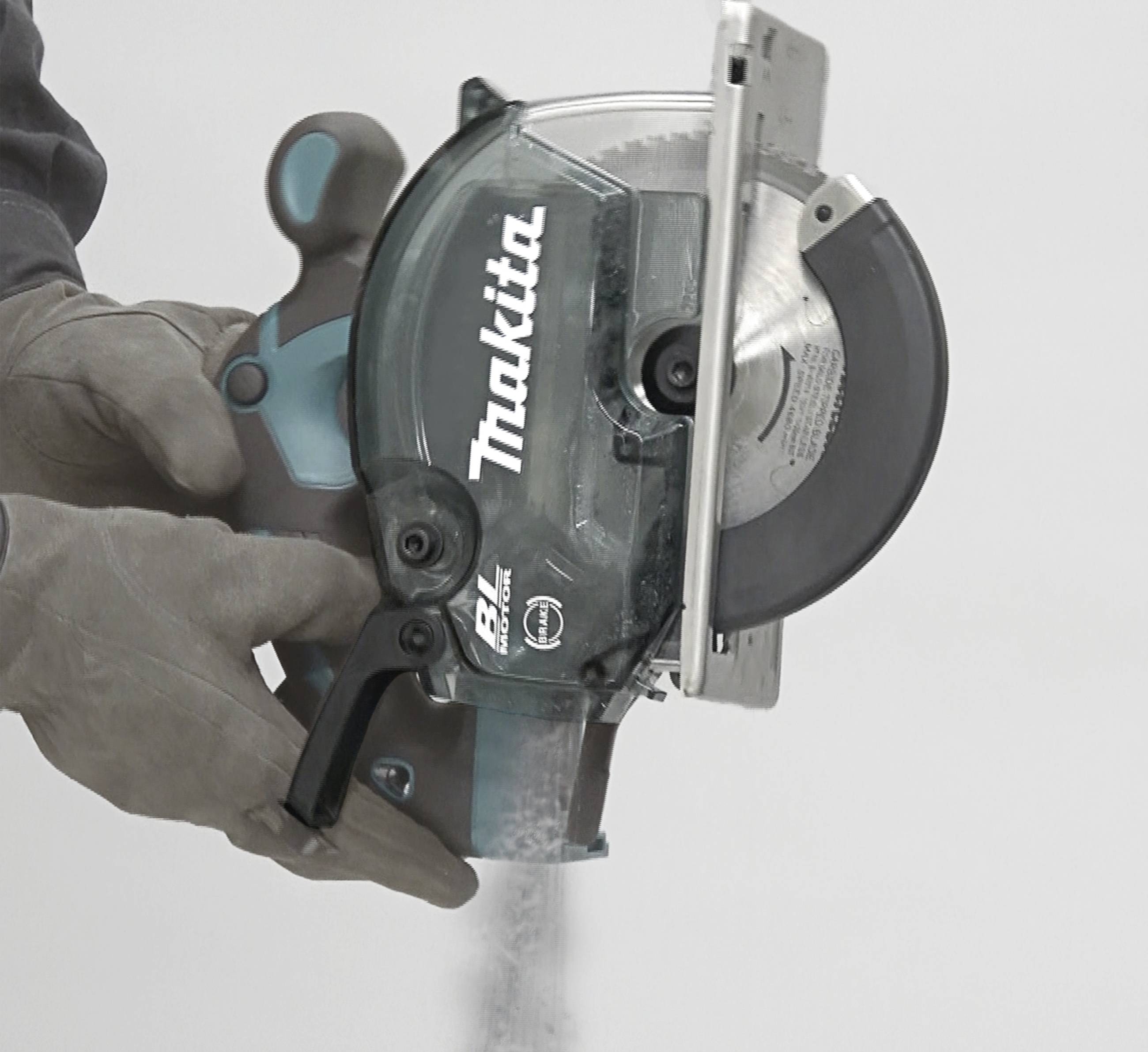 Eine Hand hält eine Kreissäge der Marke Makita. Die Säge schneidet durch Material mit aufgewirbeltem Staub.