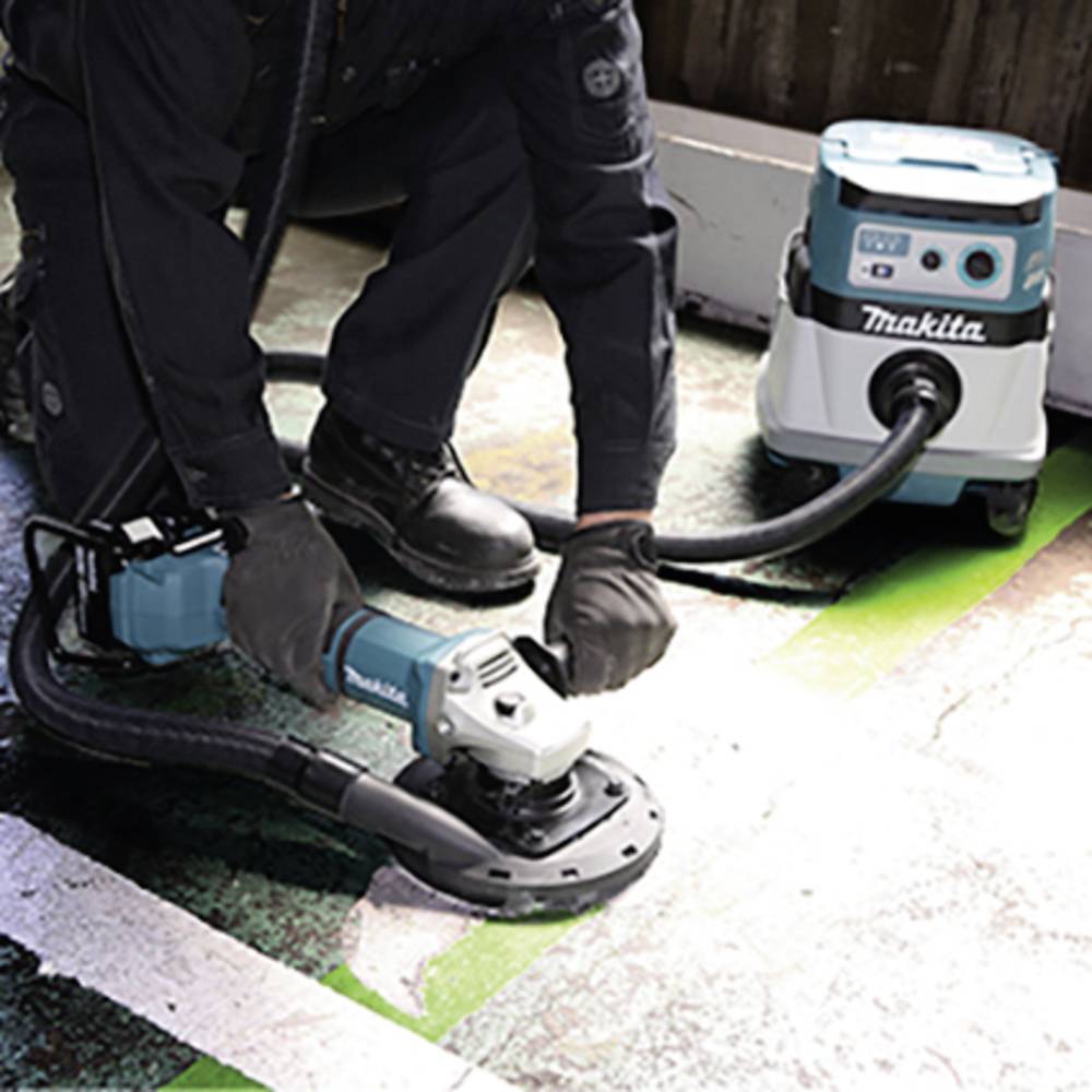 Eine Person benutzt eine elektrische Schleifmaschine mit angeschlossenem Staubsauger auf einem Boden. Im Hintergrund ein Makita-Sauger.