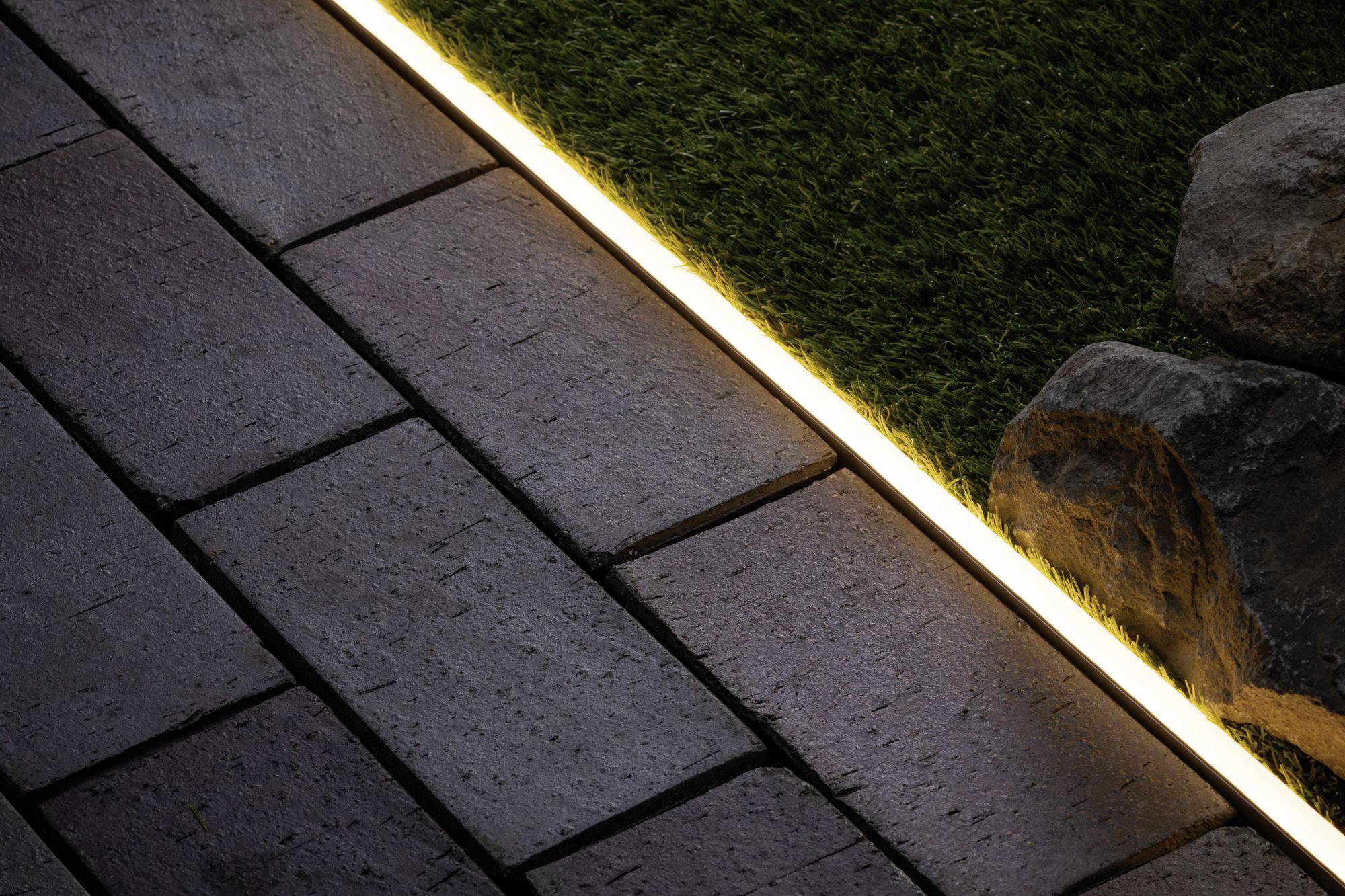Gartenbeleuchtung zeigt warm erleuchteten LED-Streifen zwischen Terrassensteinen und Kunstrasen; schafft stimmungsvolle Atmosphäre.