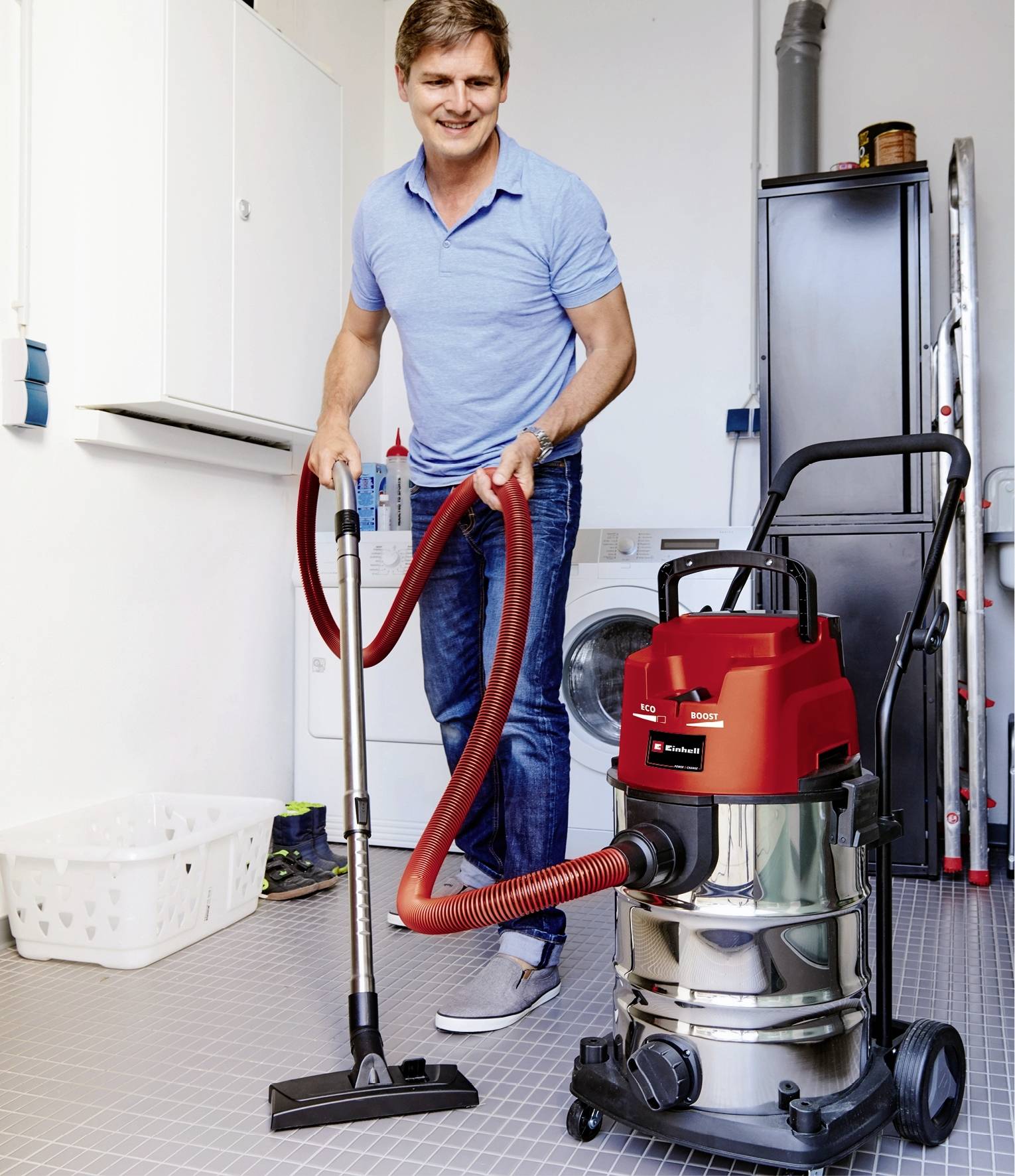 Ein Mann in lässiger Kleidung benutzt einen roten Industriestaubsauger zum Reinigen eines Hauswirtschaftsraums mit Waschmaschine.