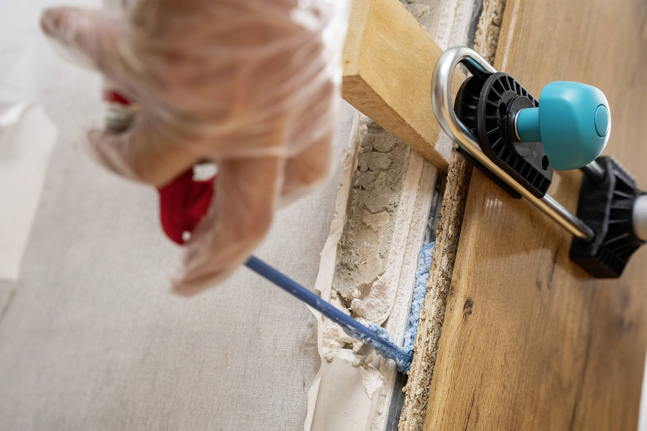 Eine Person injiziert mit einer Spritze Dichtmaterial in eine Wandritze. Eine Klemme hält ein Holzstück an der Wand.