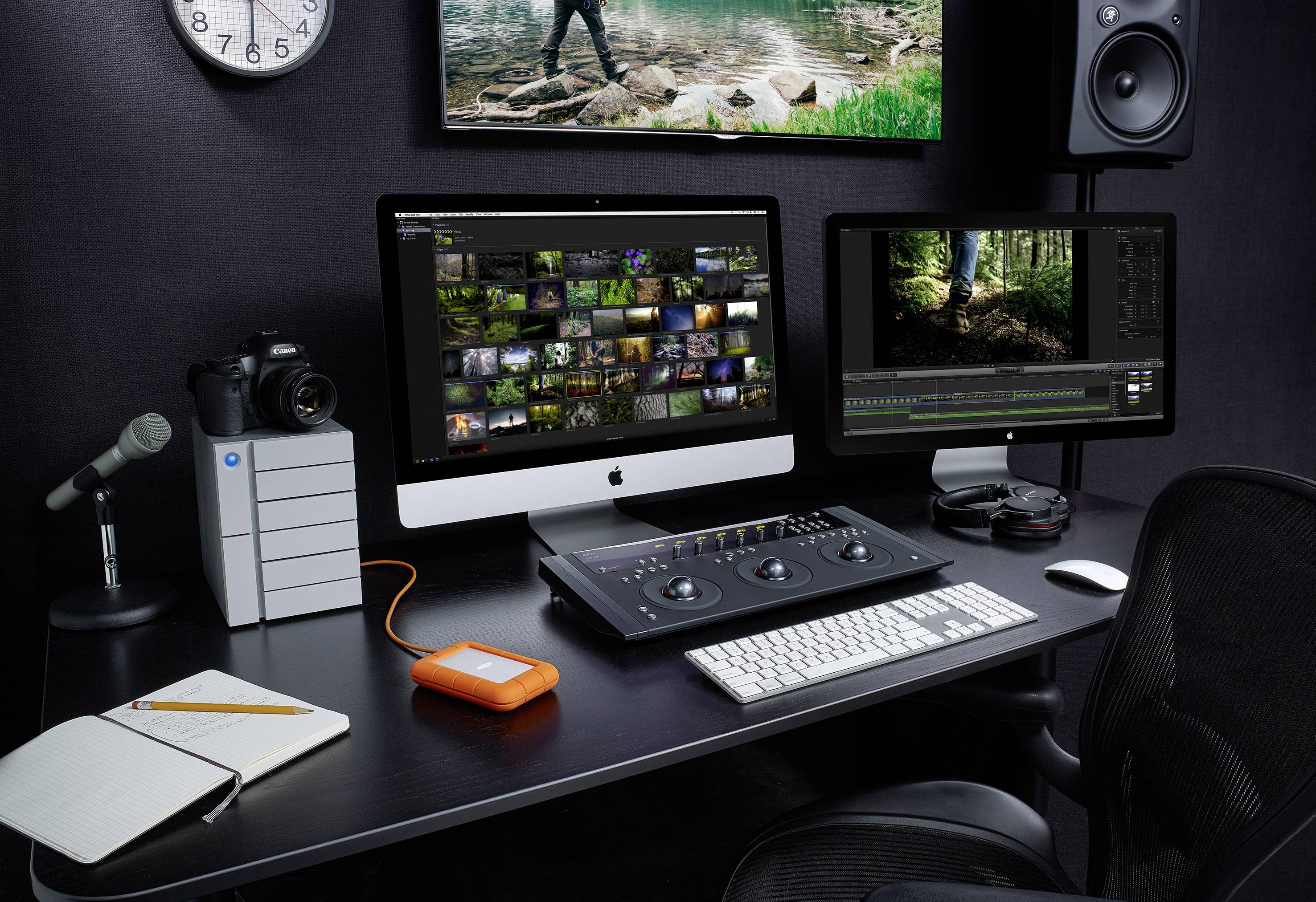 Arbeitsplatz mit zwei Monitoren, einem Audio-Mischpult, Kamera, Mikrofon, Notizbuch und externer Festplatte, geeignet für Medienbearbeitung.