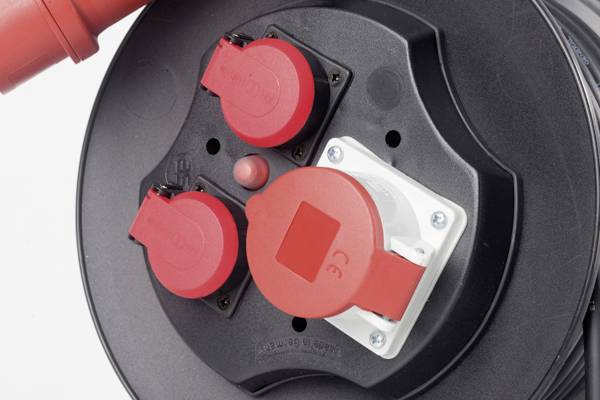 Nahaufnahme einer schwarzen Kabeltrommel mit drei roten Steckdosen und einem roten Schalter in der Mitte.
