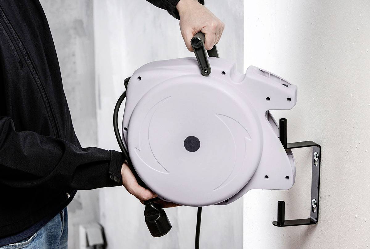 Eine Person montiert eine graue automatische Kabeltrommel an eine Wandhalterung.