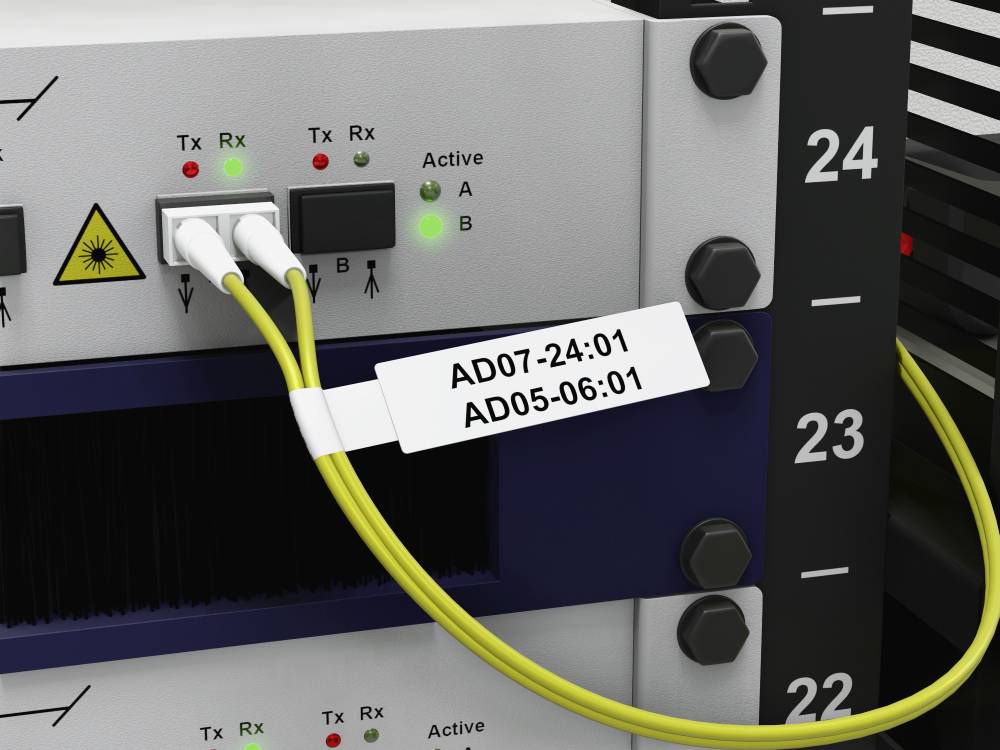 Netzwerk-Switch mit zwei gelben Glasfaserkabeln, die in die Ports A und B eingesteckt sind. Etikett zeigt AD07-24:01 und AD05-06:01.