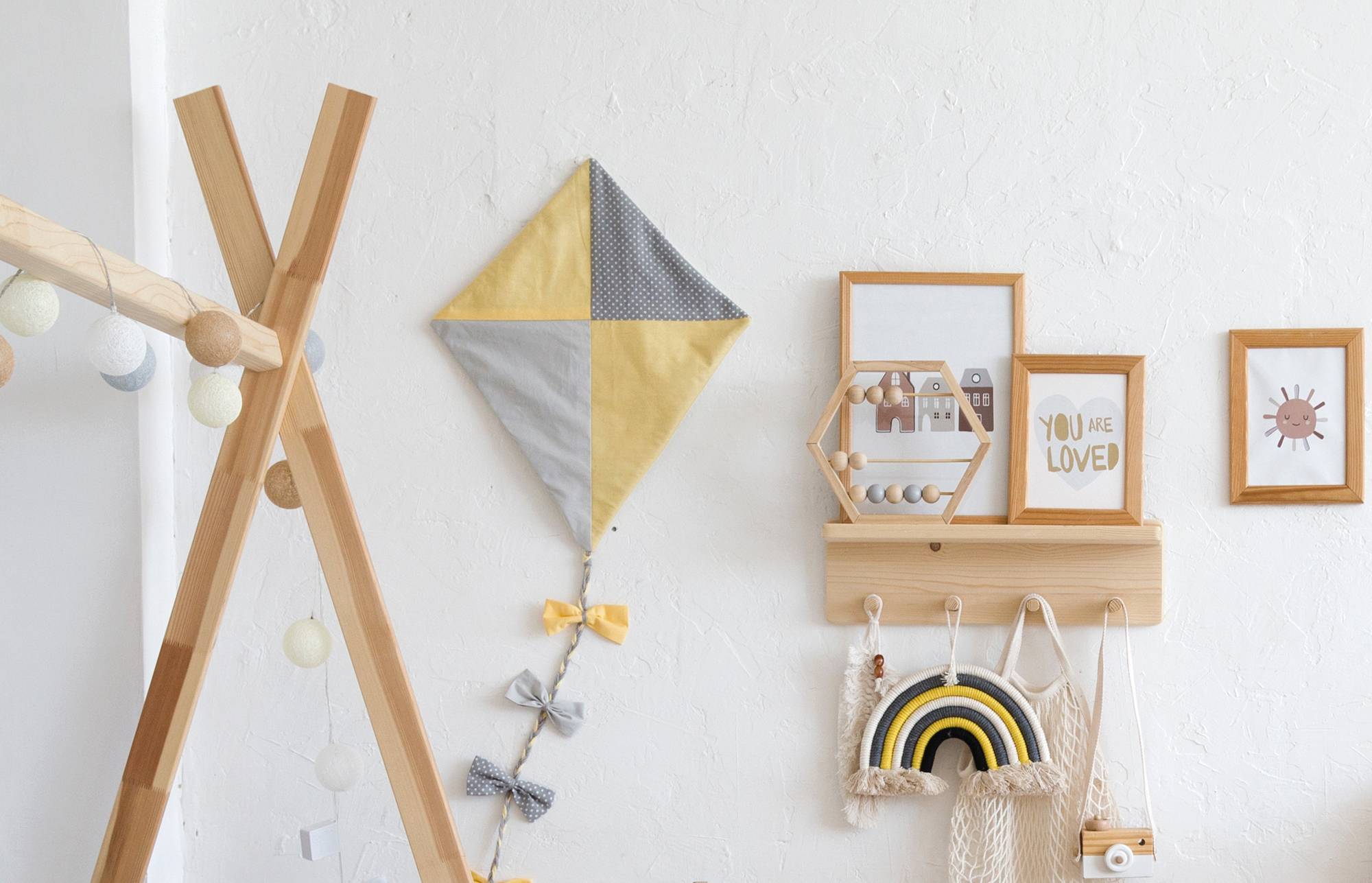 Skandinavisch inspirierte Kinderzimmer-Wanddekoration mit einem hölzernen Tipi-Regal, einem Drachen-Kite, einer hängenden Regenbogen-Tasche, gerahmter Kunst und Lichterketten.