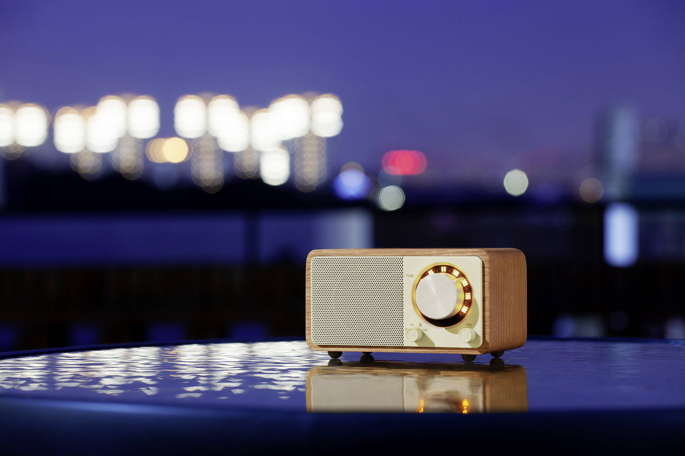 Ein Retro-Radio steht nachts auf einem glatten Tisch im Freien, beleuchtet von verschwommenen Lichtern einer Stadt im Hintergrund.