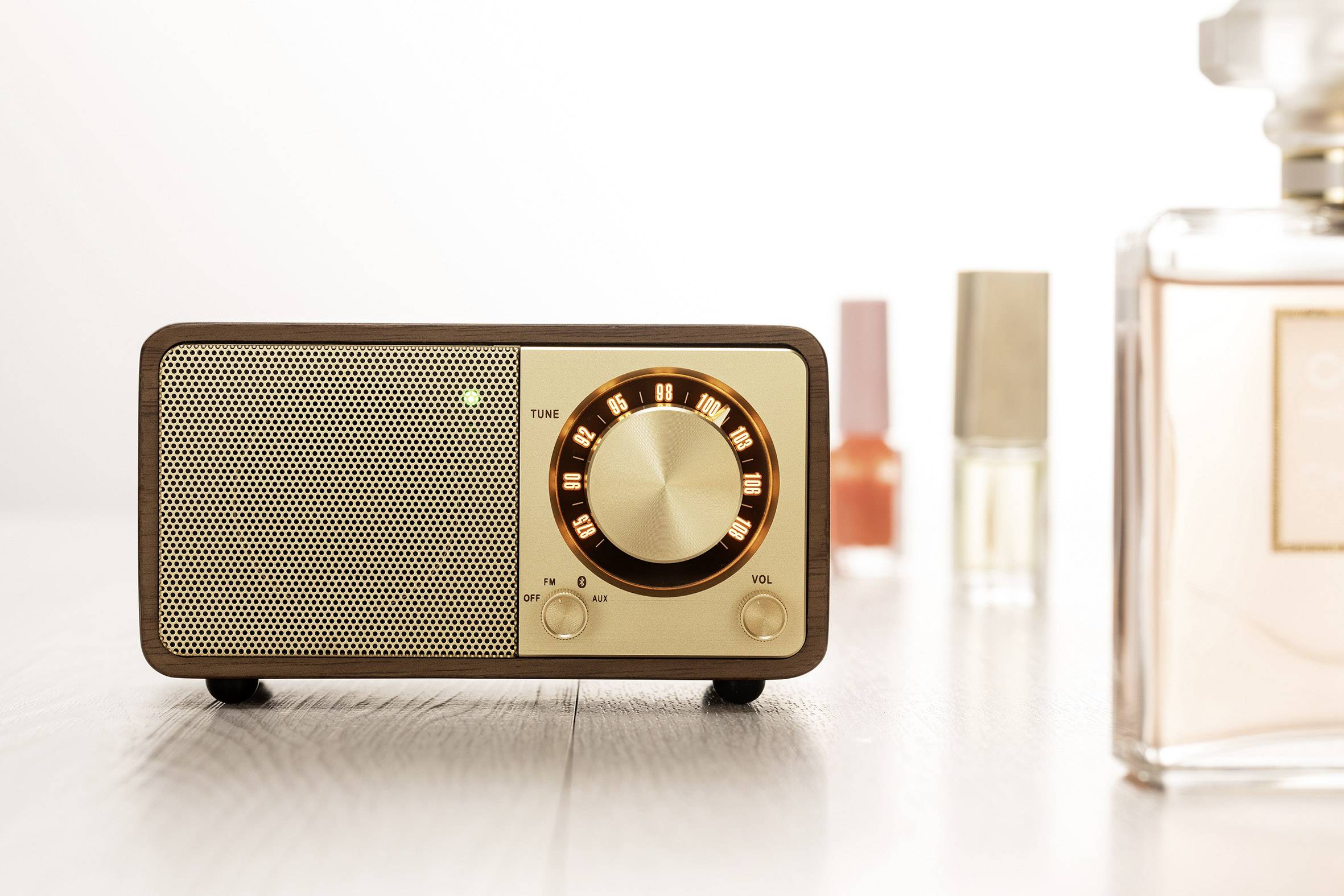 Ein Retro-Radio mit beleuchtetem Drehknopf steht auf einem Tisch. Im Hintergrund sind Teile von Parfümflaschen zu sehen.