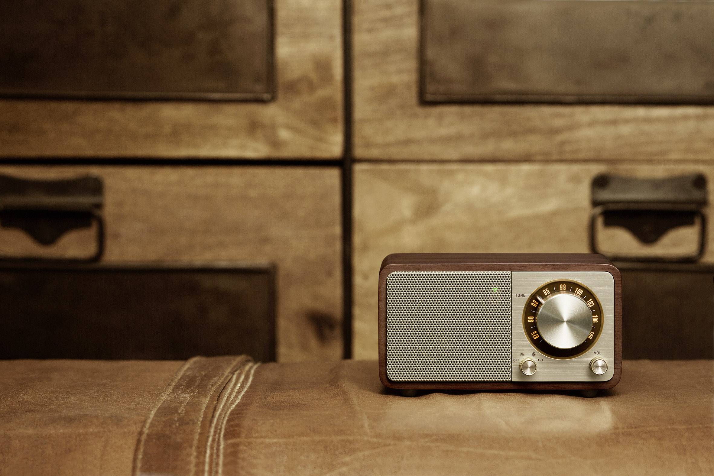 Ein Retro-Radio steht auf einem Ledersessel, im Hintergrund sind hölzerne Schubladen zu sehen. Atmosphärisches Vintage-Flair.