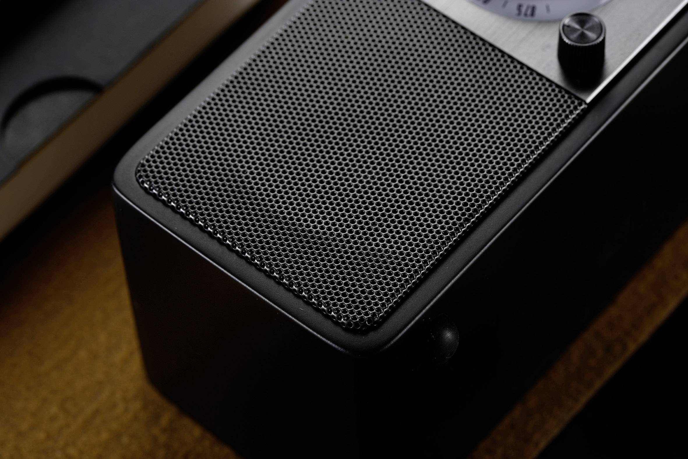Schwarzes Retro-Radio mit sichtbarem Lautsprechergitter und einem Knopf, auf einem Holztisch platziert.
