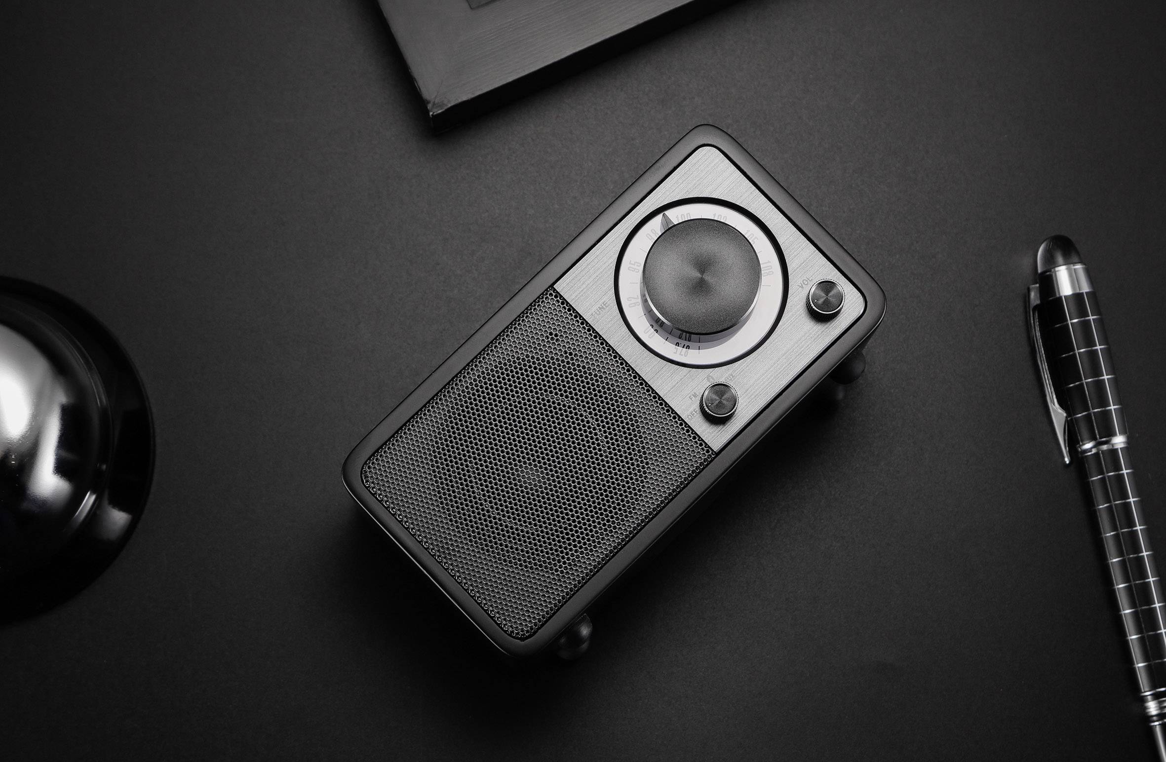 Ein kleiner schwarzer tragbarer Lautsprecher auf einem Tisch. Daneben liegt ein schwarz-silberner Stift.