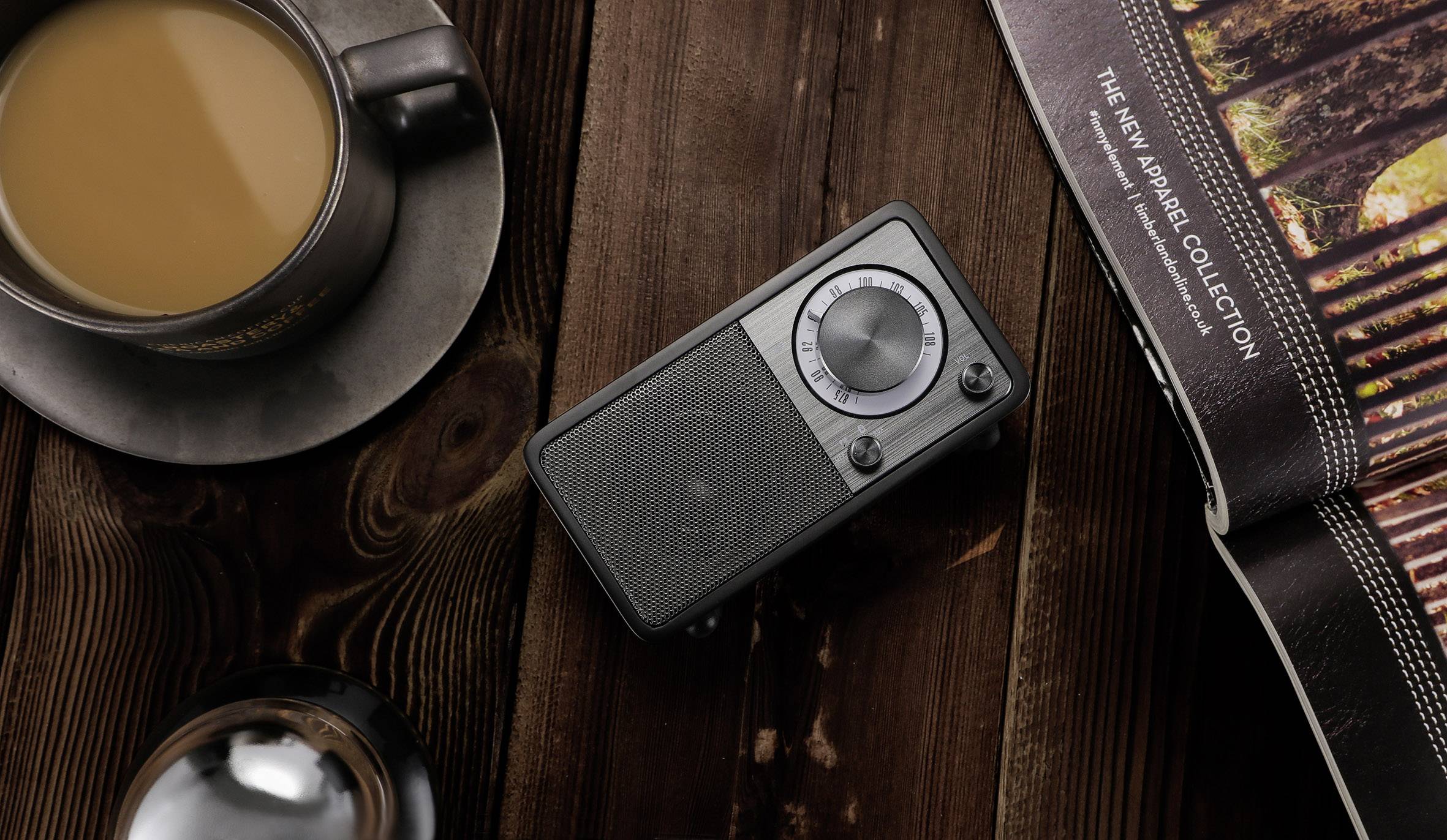 Kaffee, Radio und Zeitschrift auf Holztisch; gemütliche Szenerie für Entspannung und Lesen.