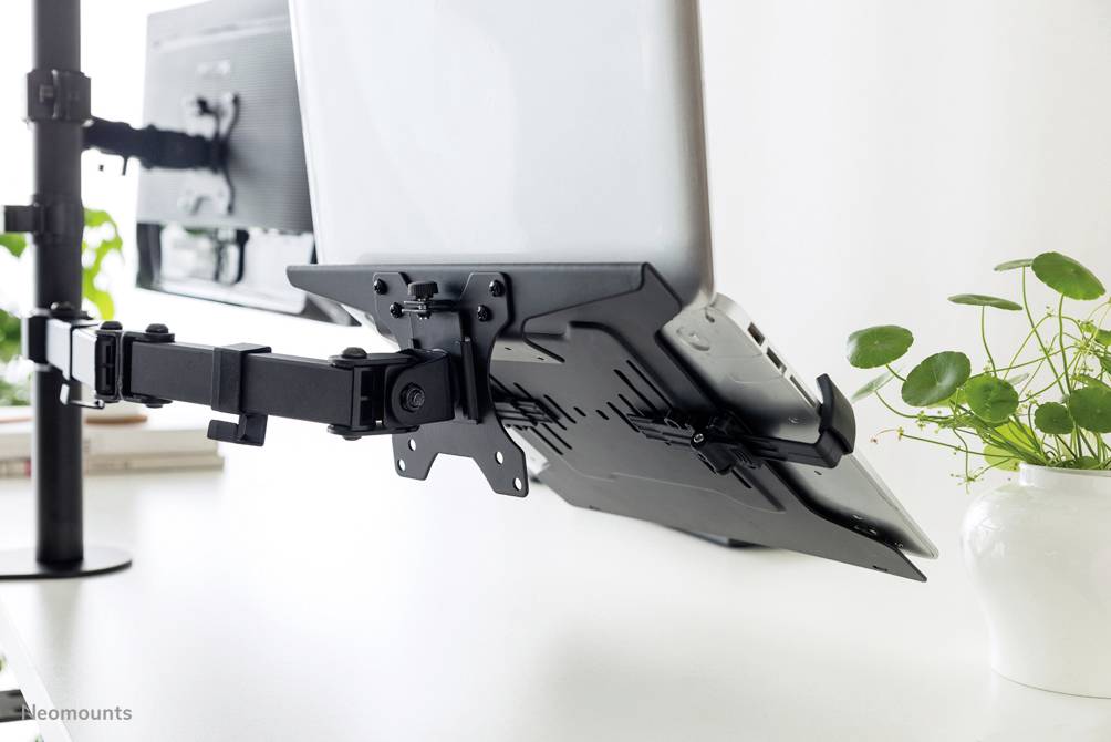 Laptop-Halterung an einem verstellbaren Arm, der an einem Schreibtisch befestigt ist, mit Pflanzen im Hintergrund. Ideal für ergonomische Arbeitsplätze.