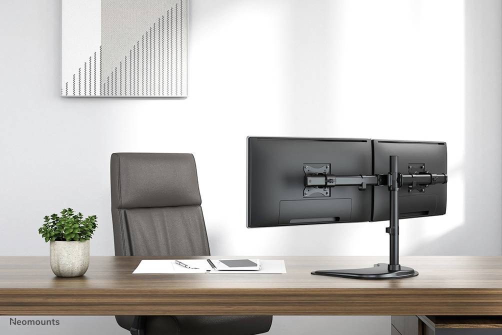 Ein modernes Büro mit dunklem Holzschreibtisch, leerem Lederstuhl, Doppelmonitorhalterung für zwei Monitore und kleinem Pflanzentopf.