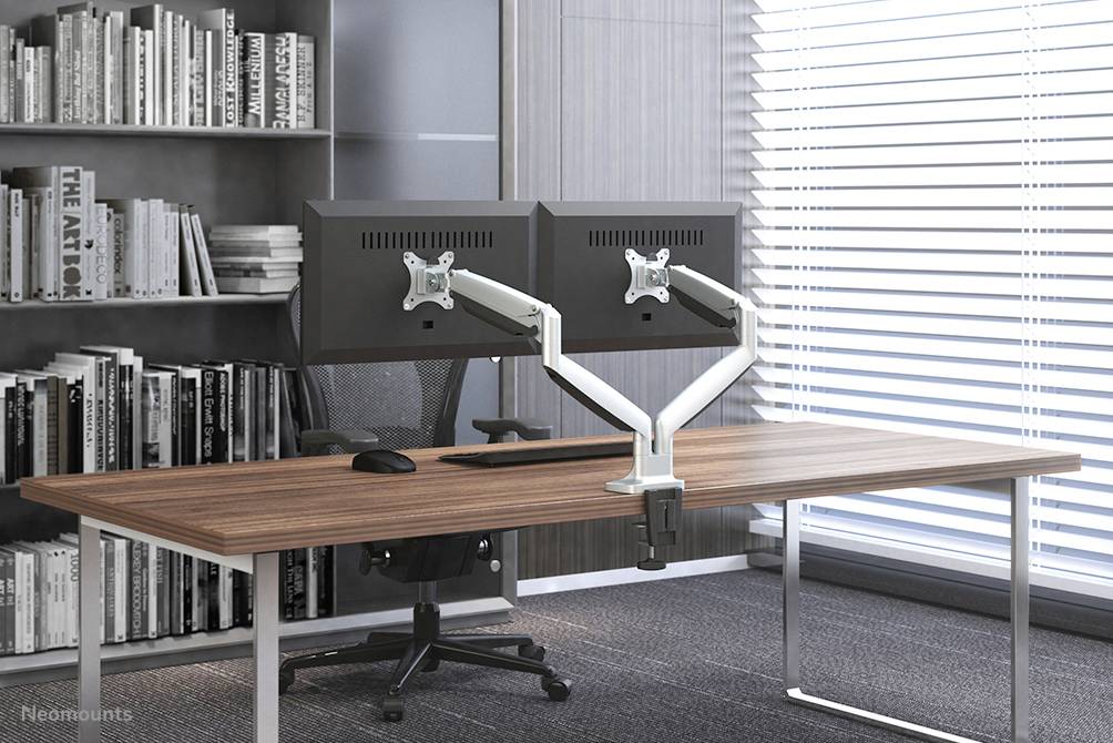 Ein moderner Schreibtisch mit zwei Monitoren auf Halterungen, einem schwarzen Bürostuhl und einem Bücherregal im Hintergrund.