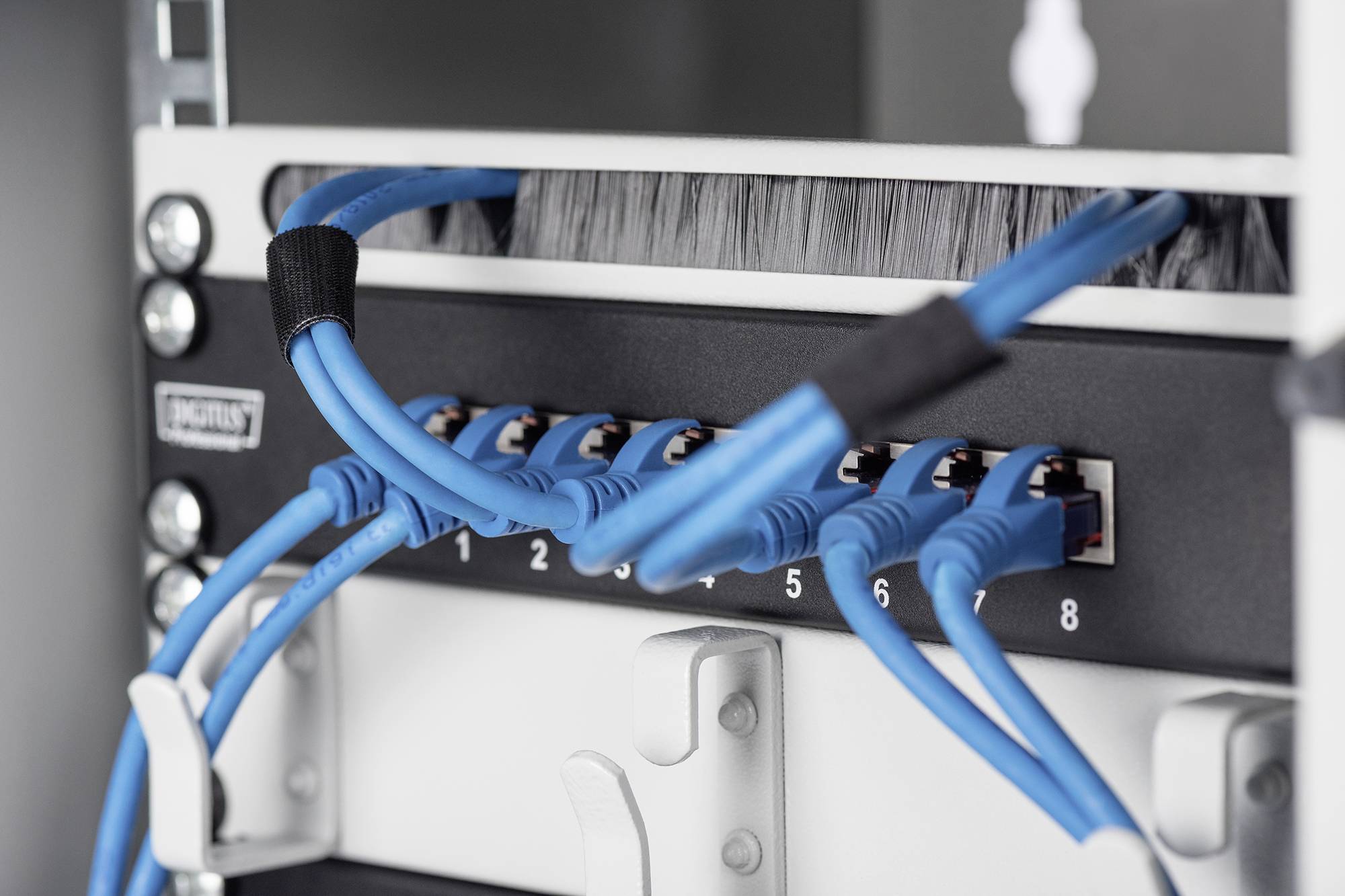 Ein Netzwerk-Server-Rack mit mehreren blauen Ethernet-Kabeln, die in nummerierte Ports eingesteckt sind. Kabel sind ordentlich organisiert.