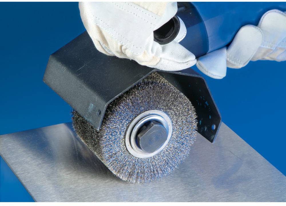 Eine rotierende Drahtbürste poliert eine Metalloberfläche. Schutzvorrichtung und Arbeitshandschuhe sind sichtbar, blaue Hintergrund.