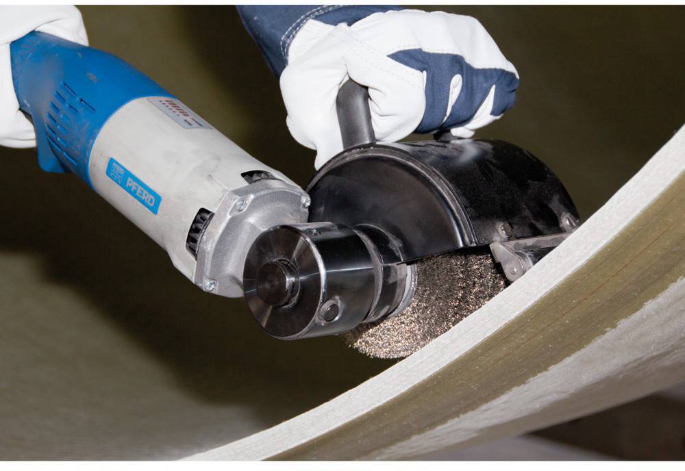 Eine Person trägt Arbeitshandschuhe und hält ein Elektrowerkzeug, das eine Metalloberfläche schleift oder poliert.