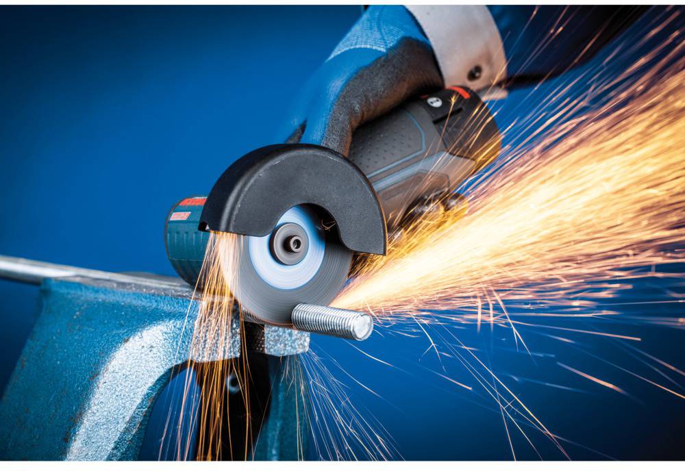 Eine Hand hält einen Winkelschleifer, der einen Metallbolzen schneidet, während Funken sprühen. Der Hintergrund ist blau.