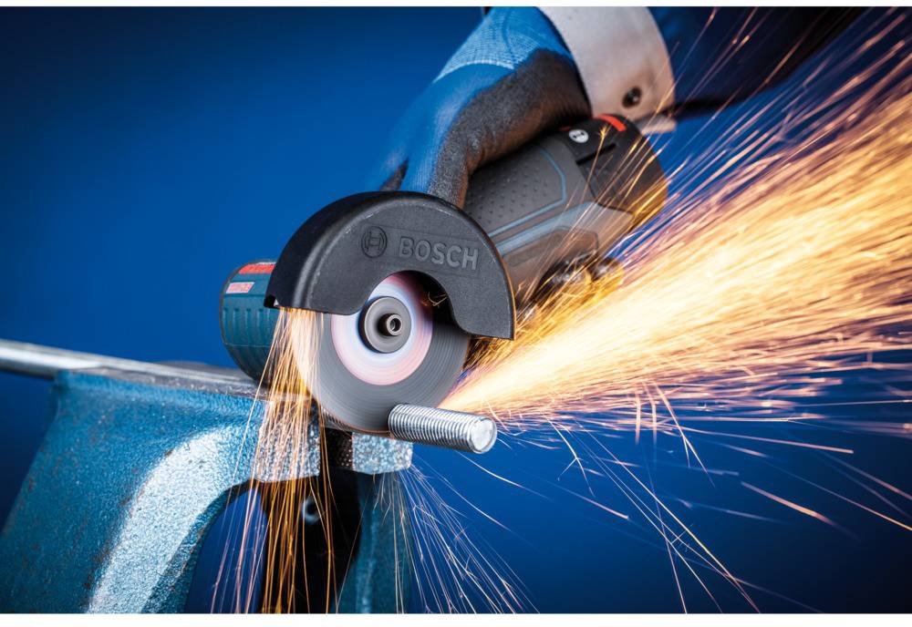 Eine Hand hält einen Winkelschleifer, der Funken sprühend eine Metallschraube schneidet. Schutzkleidung, wie Handschuhe, wird getragen.