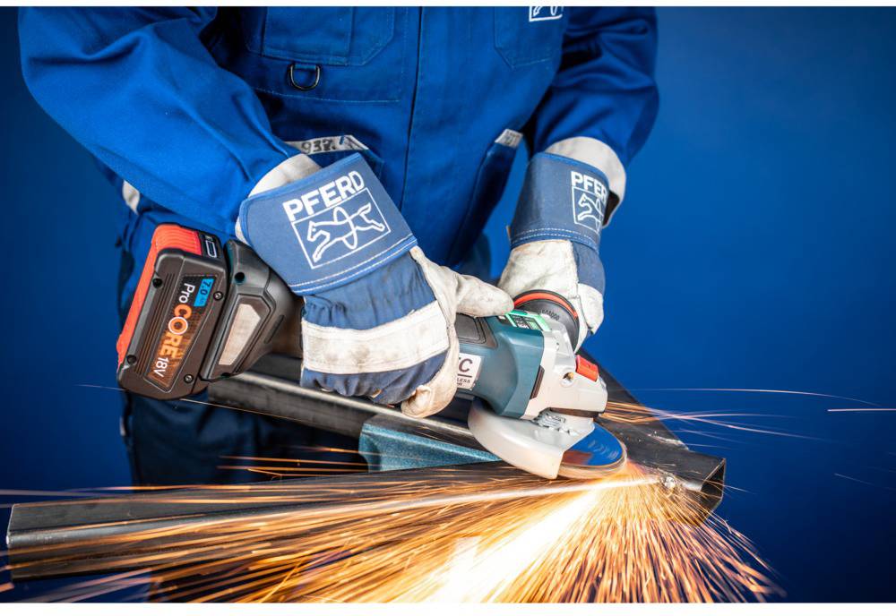 Eine Person in blauer Schutzkleidung schleift Metall mit einem elektrischen Winkelschleifer, Funken fliegen in verschiedene Richtungen.