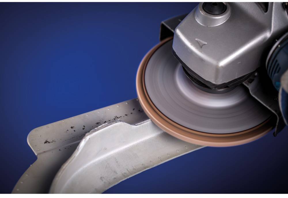 Eine Schleifmaschine bearbeitet einen Metallrand. Der Schleifstein dreht sich schnell, um die Kante zu glätten oder zu schärfen.