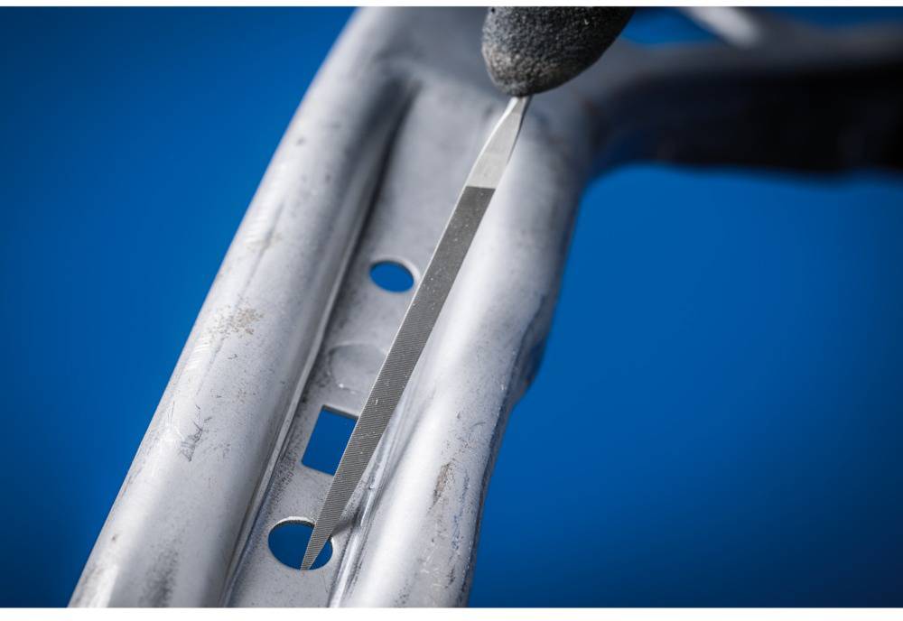 Nahaufnahme eines Metallprofils mit Löchern. Ein Handwerkzeug wird zur Bearbeitung angesetzt.