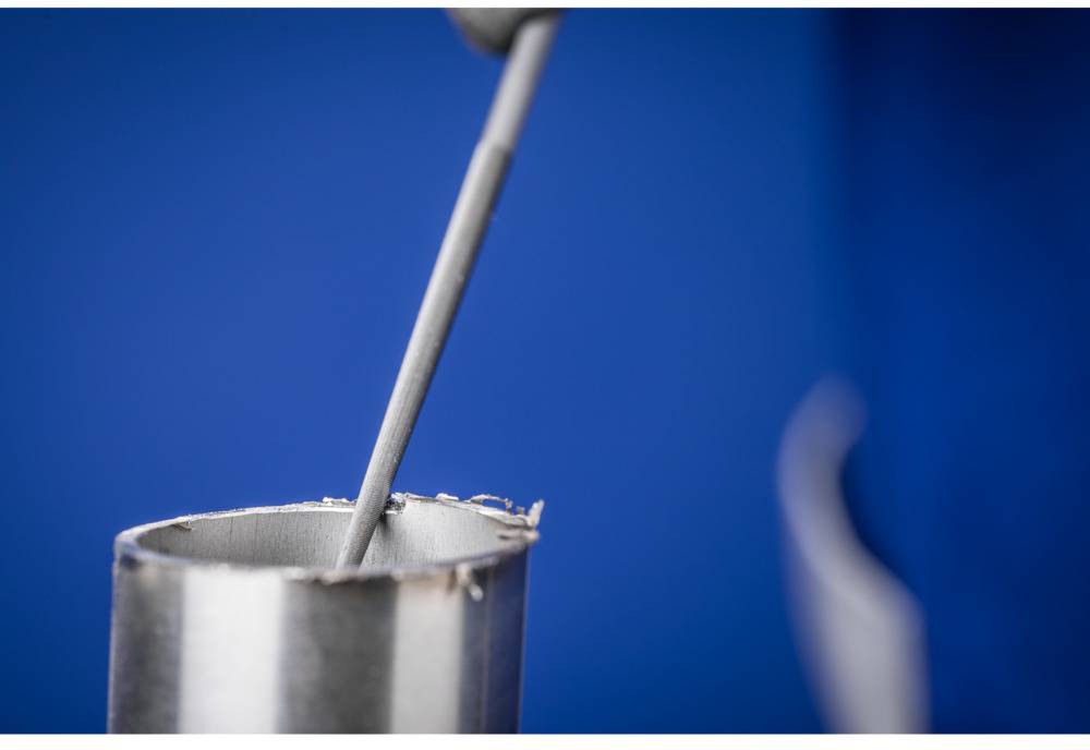 Nahaufnahme eines Röhrenbogenschweißgeräts mit blauem Hintergrund. Ein Metallstab wird in das Gerät eingeführt.