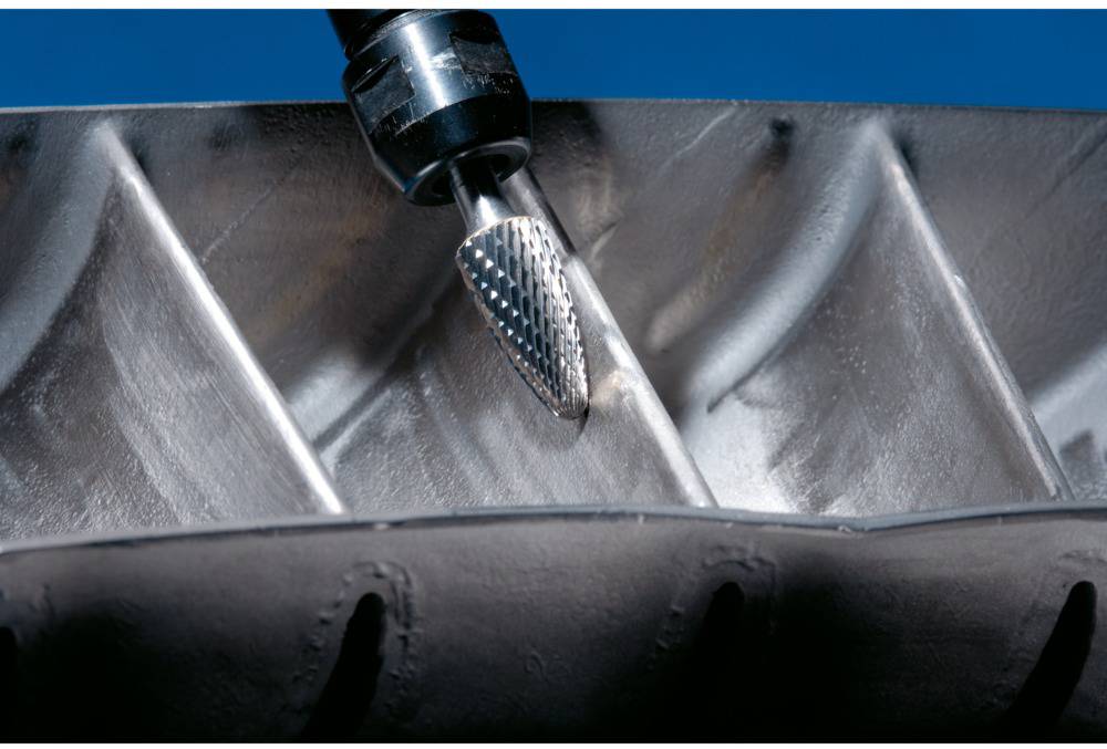 Ein Schleifwerkzeug bearbeitet eine metallische Oberfläche mit präzisen Rillen. Hauptaugenmerk liegt auf dem Materialabtragungsprozess.