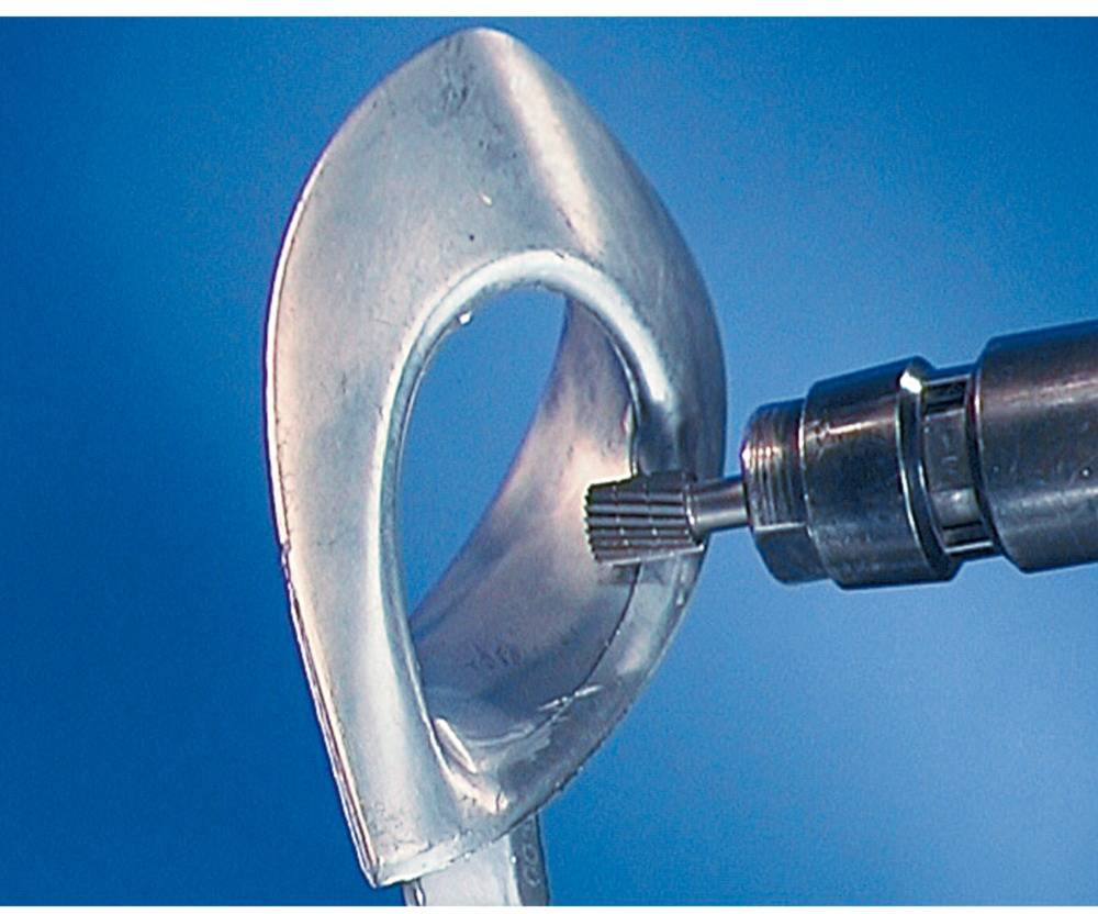 Ein Bohrer bearbeitet eine Metalloberfläche gegen einen blauen Hintergrund. Fokus auf Präzision und technische Bearbeitung.