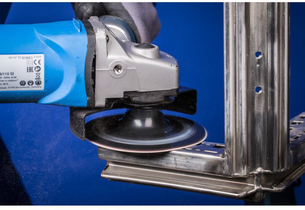 Eine Person schleift ein Metallstück mit einem Winkelschleifer. Funken fliegen durch die Reibung. Sicherheitsausrüstung wird verwendet.