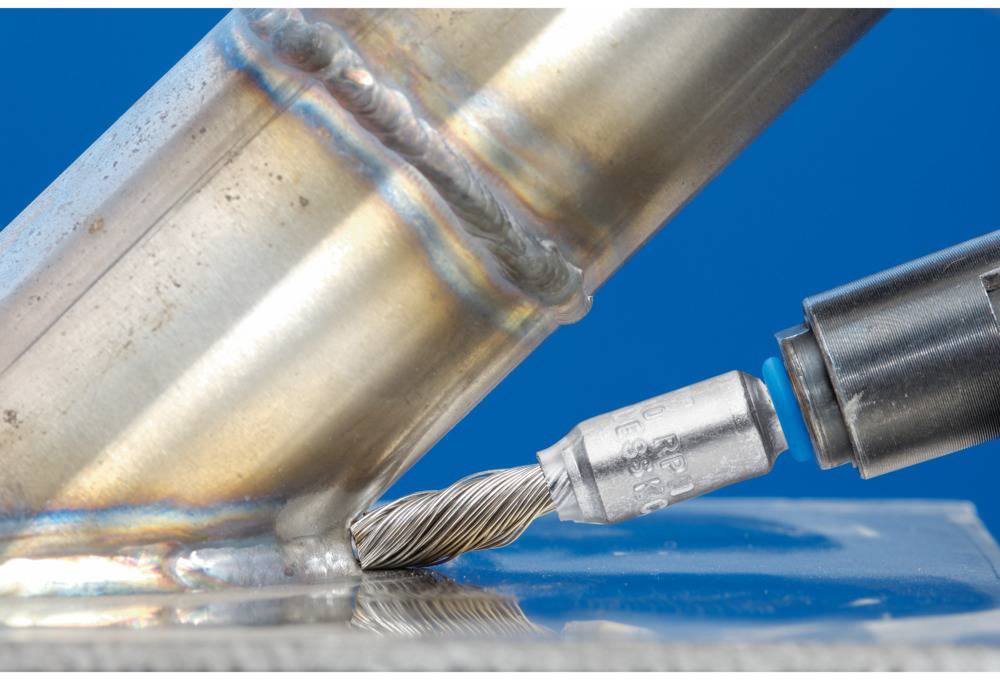 Ein Fräser bearbeitet eine Metallnaht an einem Rohr. Die Spitze des Werkzeugs zeigt in die Schweißnaht, blaue Hintergrundfarbe.