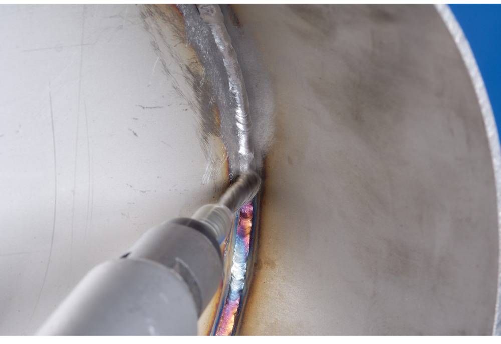 Eine Nahaufnahme zeigt eine Schweißnaht an einem Metallzylinder. Ein Werkzeug berührt die Schweißnaht, um sie zu bearbeiten oder zu überprüfen.