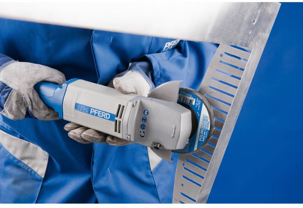 Person in blauer Arbeitskleidung hält eine elektrische Schleifmaschine, die eine Metallfläche schleift.